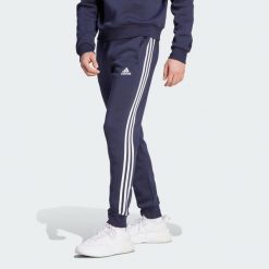 Spodnie Essentials Fleece 3-Stripes Tapered Cuff. Białe spodnie sportowe męskie Adidas, z materiału. Za 229.00 zł.