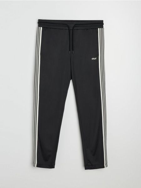 Spodnie dresowe z ozdobnymi taśmami po boku - czarny. Czarne spodnie sportowe męskie Sinsay, z dresówki. Za 59.99 zł.