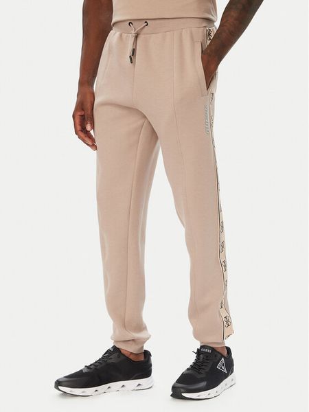 Guess Spodnie dresowe Z2YB09 KB3P2 Beżowy ciemny Regular Fit. Brązowe spodnie dresowe męskie Guess, z aplikacjami, z dresówki. Za 434.99 zł.