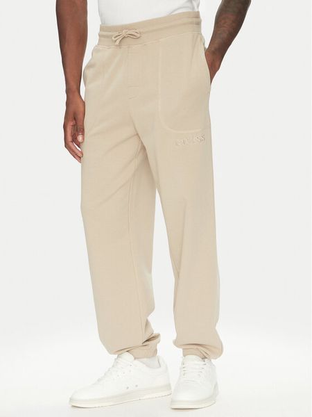 Guess Spodnie dresowe U5RB00 KCO31 Beżowy Regular Fit. Brązowe spodnie dresowe męskie Guess, z aplikacjami, z bawełny. Za 159.99 zł.