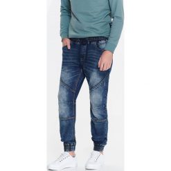 SPODNIE MĘSKIE TYPU JOGGER Z DZIANINY IMITUJĄCEJ JEANS. Niebieskie spodnie materiałowe męskie TOP SECRET, bez wzorów, z dzianiny. W wyprzedaży za 64.99 zł.