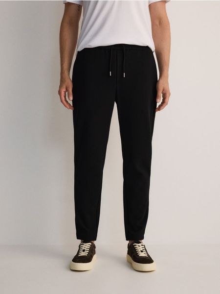 Spodnie slim fit z wiązaniem - czarny. Czarne spodnie materiałowe męskie Reserved, bez wzorów, z bawełny. W wyprzedaży za 59.99 zł.
