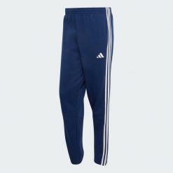 Spodnie Essentials z tkaniny frotté z 3 paskami i zwężanymi nogawkami. Białe spodnie materiałowe męskie Adidas, bez wzorów, z bawełny, klasyczne, z standardowym stanem. Za 219.00 zł.