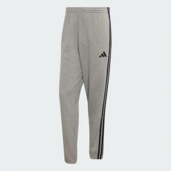 Spodnie Essentials z tkaniny frotté z 3 paskami i zwężanymi nogawkami. Białe spodnie materiałowe męskie Adidas, bez wzorów, z bawełny, klasyczne, z standardowym stanem. Za 219.00 zł.